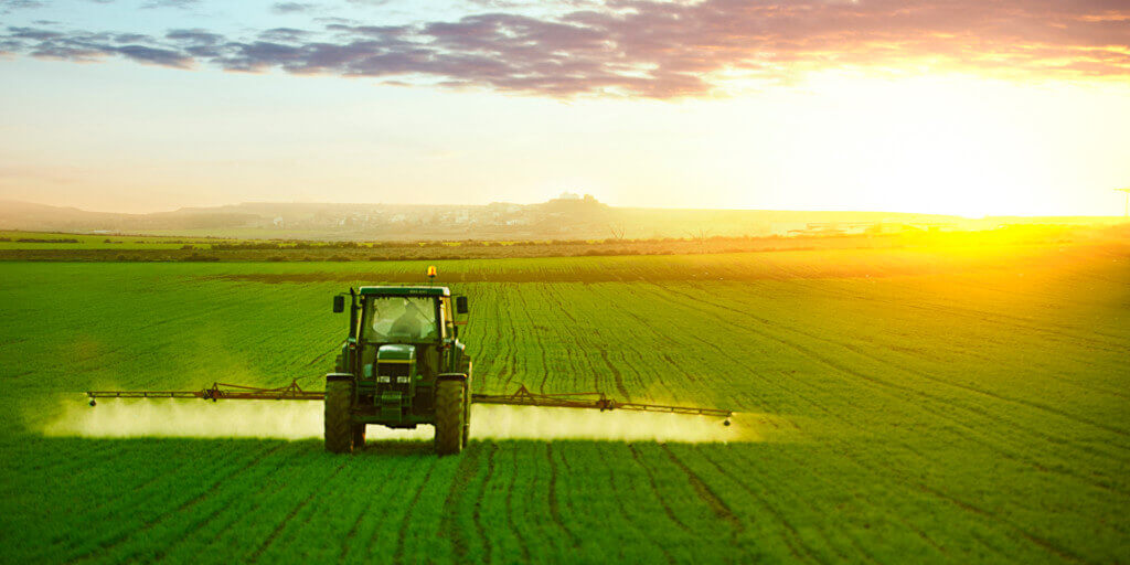 A picture of a green farm field and tractor at sunset.