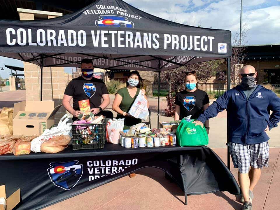 A picture of four volunteers standing under a "Colorado Veterans Project" tent holding food donations from the Memorial Day run.