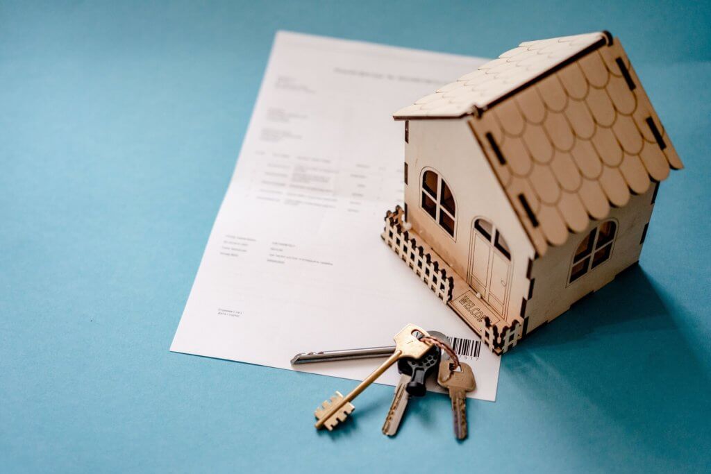 Wooden doll house sitting next to house keys and an insurance invoice.