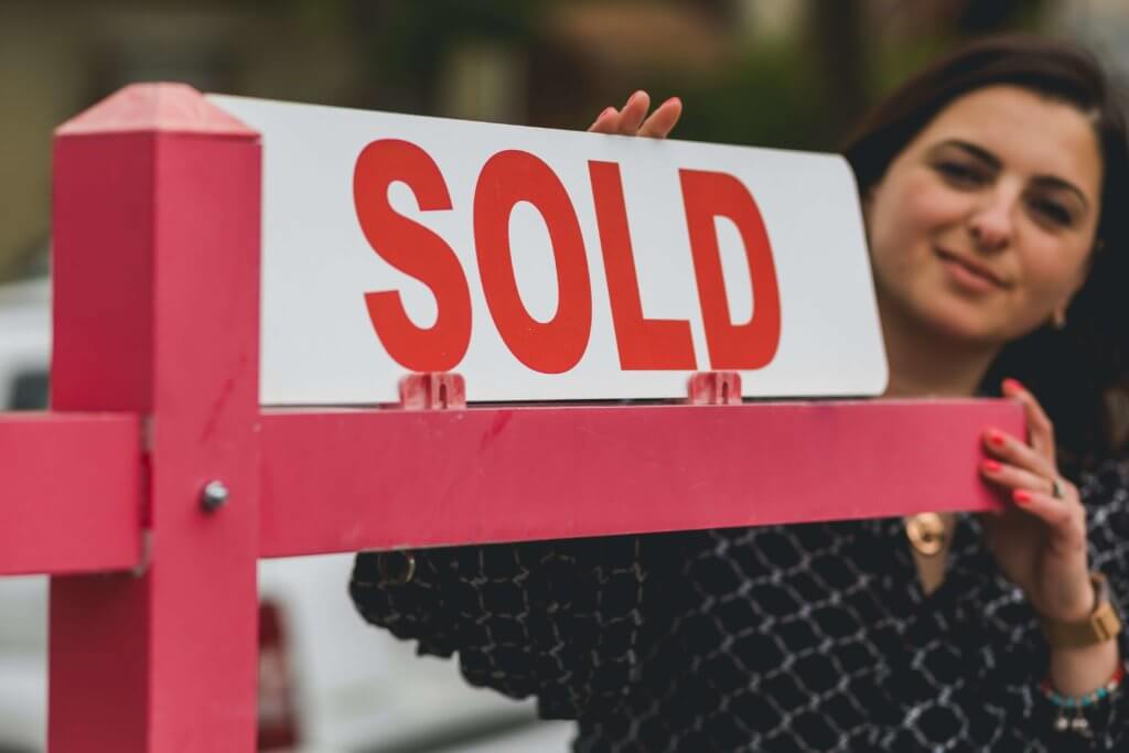 Female realtor putting up a sold sign.