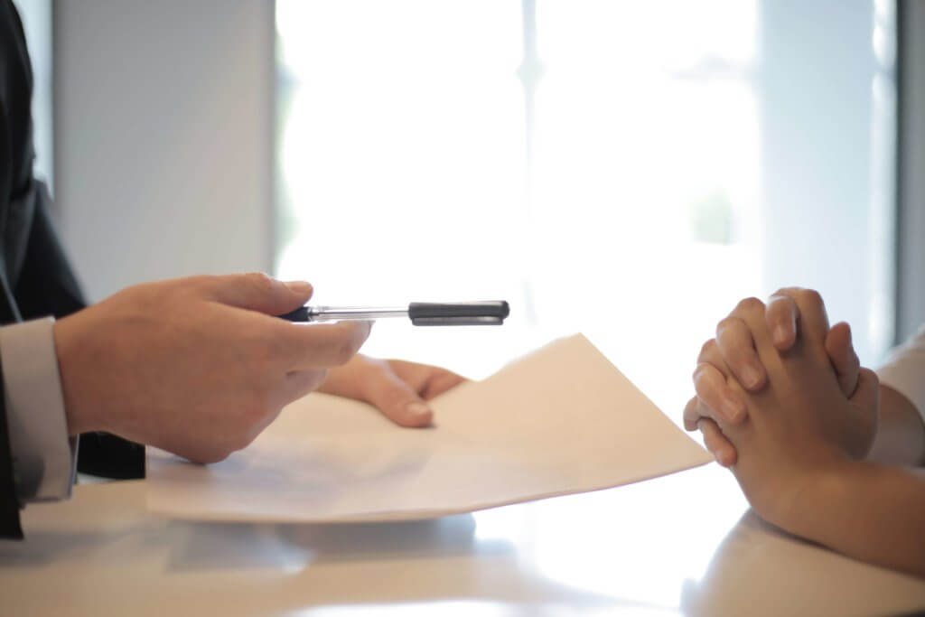 A loan officer handing a pen and conventional loan closing documents to a home buyer.